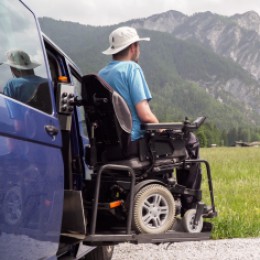 A man in an electric wheelchair being lowered in a vehicle lift. 